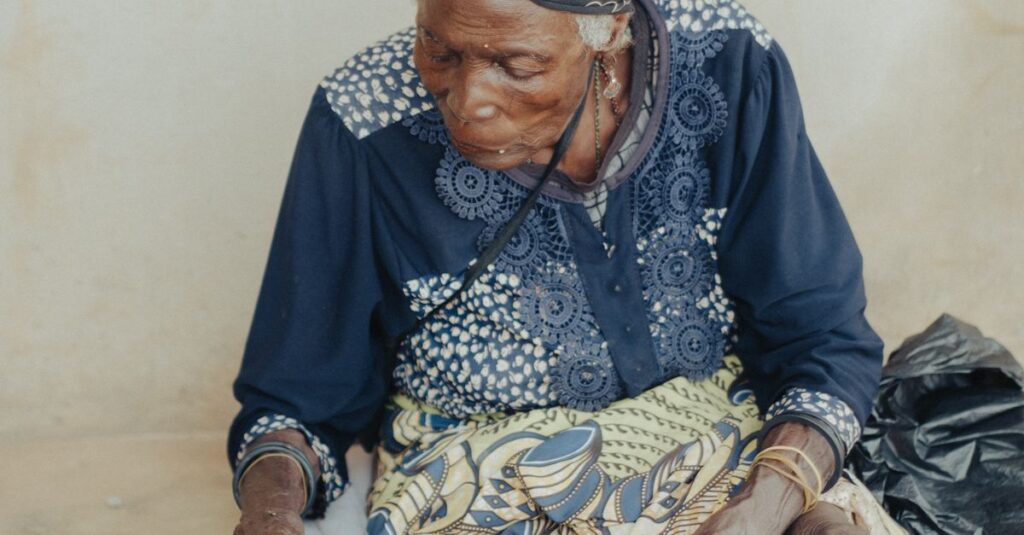 Senior woman seated and looking down inside. Wearing a patterned headscarf and traditional clothing.